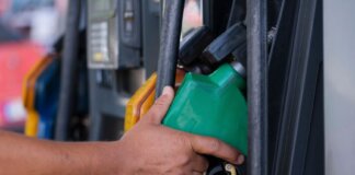 Close-up of a hand holding a green fuel nozzle at a gas pump station outdoors.