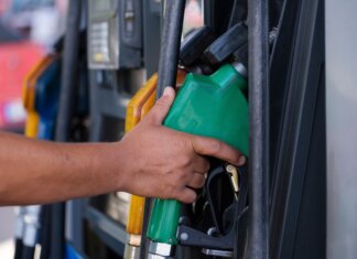 Close-up of a hand holding a green fuel nozzle at a gas pump station outdoors.