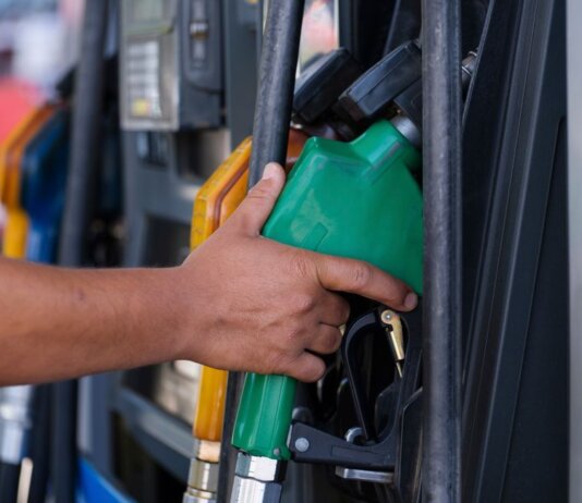 Close-up of a hand holding a green fuel nozzle at a gas pump station outdoors.