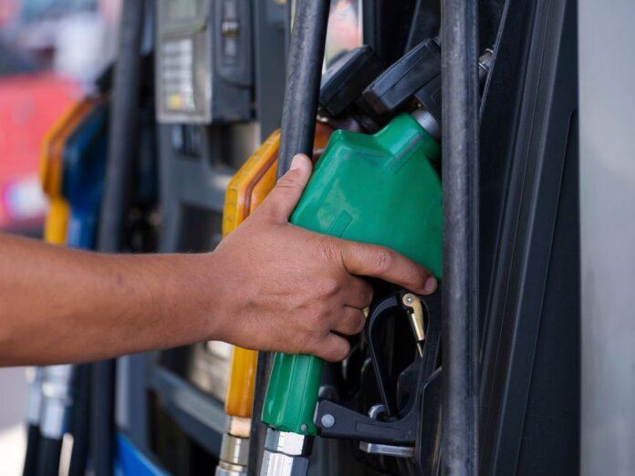 Close-up of a hand holding a green fuel nozzle at a gas pump station outdoors. Close-up of a hand holding a green fuel nozzle at a gas pump station outdoors.