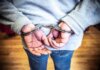 Убийство у казино в Пикеринге: подозреваемого задержали в Саскатуне спустя годы Close-up of a person in handcuffs viewed from behind, wearing casual clothing indoors.