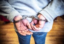 Close-up of a person in handcuffs viewed from behind, wearing casual clothing indoors.