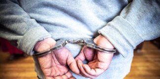 Close-up of a person in handcuffs viewed from behind, wearing casual clothing indoors.