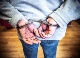 Close-up of a person in handcuffs viewed from behind, wearing casual clothing indoors.
