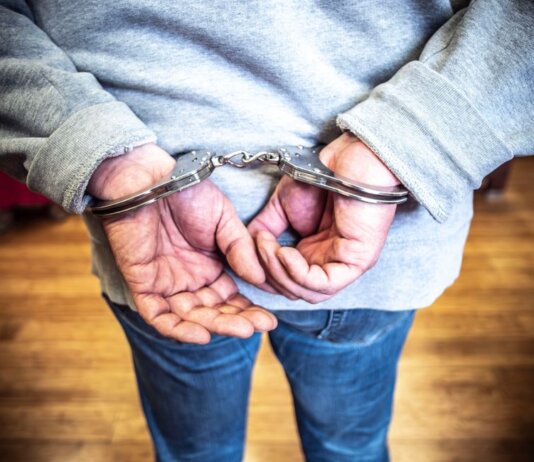 Close-up of a person in handcuffs viewed from behind, wearing casual clothing indoors.