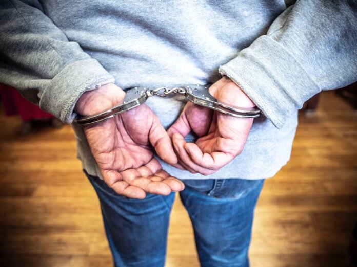 Close-up of a person in handcuffs viewed from behind, wearing casual clothing indoors. Close-up of a person in handcuffs viewed from behind, wearing casual clothing indoors.