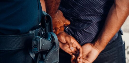 В Ошаве арестован мужчина, угрожавший ножом владельцу автомобиля Close-up of a police officer arresting a suspect with visible firearm outdoors.