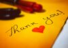 Close-up of a thank you note with a heart and pen on colored paper.