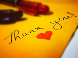 Close-up of a thank you note with a heart and pen on colored paper.