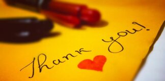 Close-up of a thank you note with a heart and pen on colored paper.