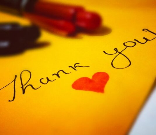 Close-up of a thank you note with a heart and pen on colored paper.