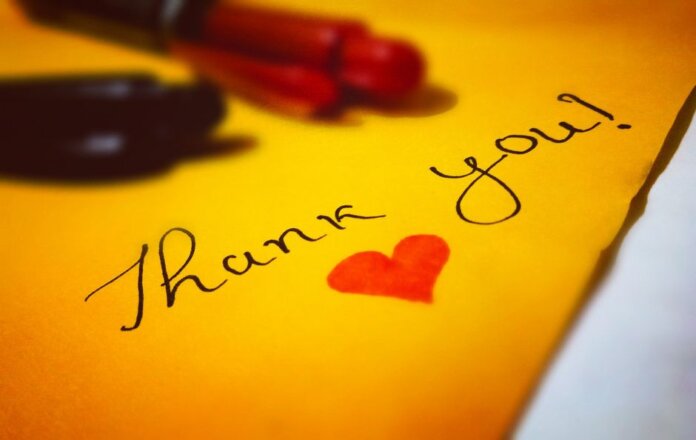 Close-up of a thank you note with a heart and pen on colored paper. Close-up of a thank you note with a heart and pen on colored paper.