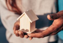 Close-up of hands holding a small wooden house, symbolizing real estate or home ownership.