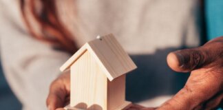 Close-up of hands holding a small wooden house, symbolizing real estate or home ownership.