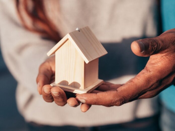 Close-up of hands holding a small wooden house, symbolizing real estate or home ownership. Close-up of hands holding a small wooden house, symbolizing real estate or home ownership.