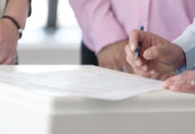 Close-up of hands signing documents in an office setting, emphasizing collaboration and decision-making.