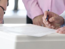 Close-up of hands signing documents in an office setting, emphasizing collaboration and decision-making.