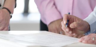 Close-up of hands signing documents in an office setting, emphasizing collaboration and decision-making.