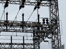 Close-up of high voltage power lines with intricate metal structures against a cloudy sky.