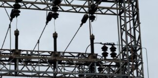 Close-up of high voltage power lines with intricate metal structures against a cloudy sky.
