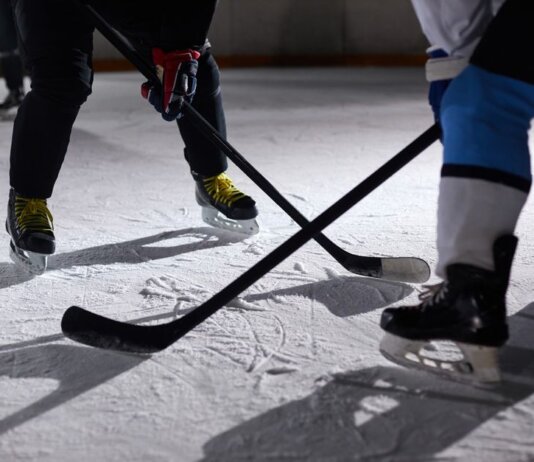 Close-up of hockey players battling for puck during an intense face-off on a lighted ice rink.