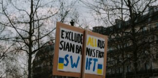Crowd gathered with placards during a protest against Russian banks in an urban setting.