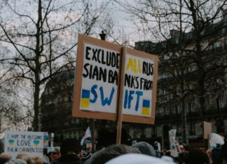 Crowd gathered with placards during a protest against Russian banks in an urban setting.