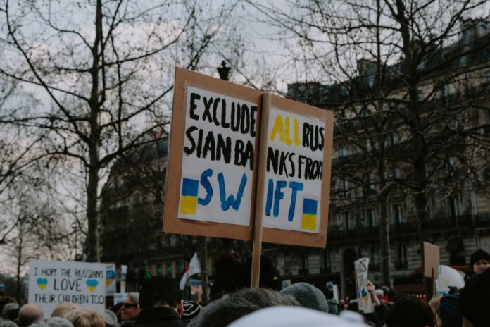 Crowd gathered with placards during a protest against Russian banks in an urban setting. Crowd gathered with placards during a protest against Russian banks in an urban setting.
