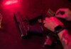 Dramatic close-up of a tattooed hand loading bullets beside a handgun and whiskey glass.