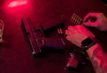 В Боуманвилле при остановке автомобиля полиция изъяла заряженный пистолет Dramatic close-up of a tattooed hand loading bullets beside a handgun and whiskey glass.