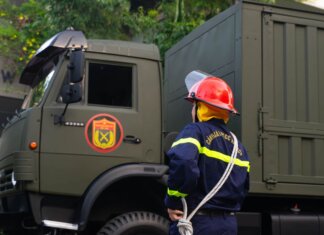 Firefighter in uniform with protective gear stands by an army truck outdoors.