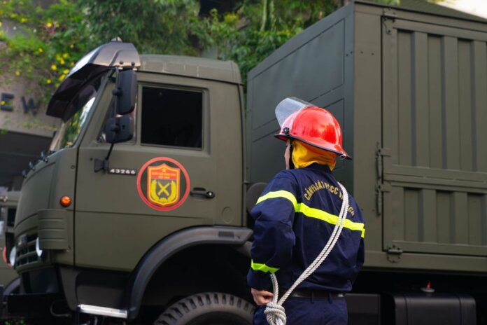 Firefighter in uniform with protective gear stands by an army truck outdoors. Firefighter in uniform with protective gear stands by an army truck outdoors.