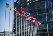 Flags of European Union countries outside a modern building facade.