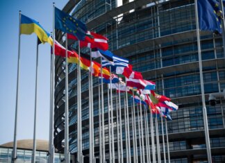 Flags of European Union countries outside a modern building facade.