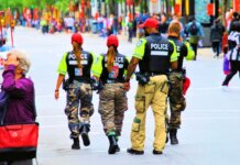 Group of police officers in uniform patrolling a crowded city street on a sunny day.