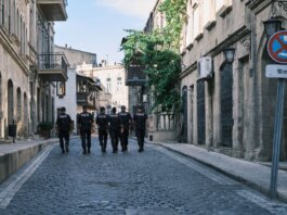 Group of policemen strolling through a historic European city street on a sunny day.