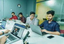 Group of young professionals working together in a modern office setting, using laptops and technology.
