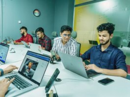 Group of young professionals working together in a modern office setting, using laptops and technology.
