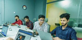 Group of young professionals working together in a modern office setting, using laptops and technology.