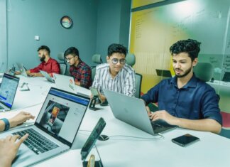 Group of young professionals working together in a modern office setting, using laptops and technology.