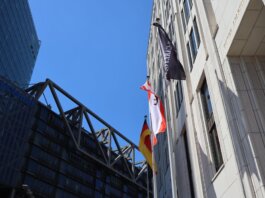 Low angle view of modern buildings in Berlin with flags against blue sky.