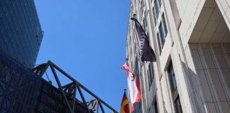 Low angle view of modern buildings in Berlin with flags against blue sky.