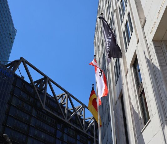 Low angle view of modern buildings in Berlin with flags against blue sky.