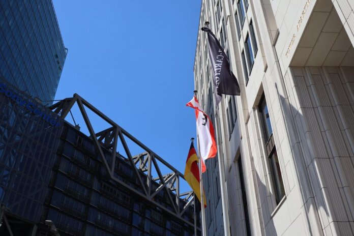 Low angle view of modern buildings in Berlin with flags against blue sky.