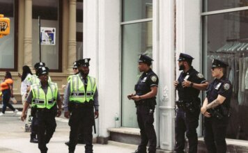 На посту Куттс в Альберте изъяли более 215 кг кокаина из двух фур NYPD officers in uniform monitor a busy city street in daytime, ensuring public safety.