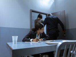 Police officer escorting suspect as lawyer observes during interrogation.