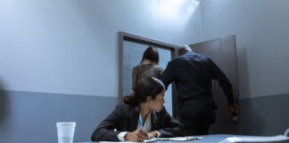 Police officer escorting suspect as lawyer observes during interrogation.