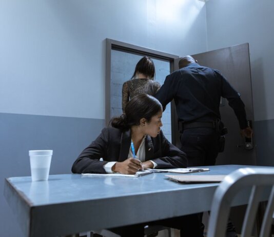 Police officer escorting suspect as lawyer observes during interrogation.