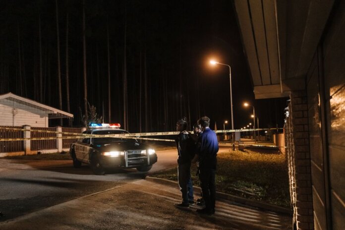 Police officers at a nighttime crime scene with a police car and caution tape under streetlights. Police officers at a nighttime crime scene with a police car and caution tape under streetlights.