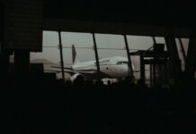 Консерваторы требуют от Air Canada обслуживать пассажиров на двух официальных языках Silhouette of an airplane and waiting passengers inside an airport terminal at dusk.